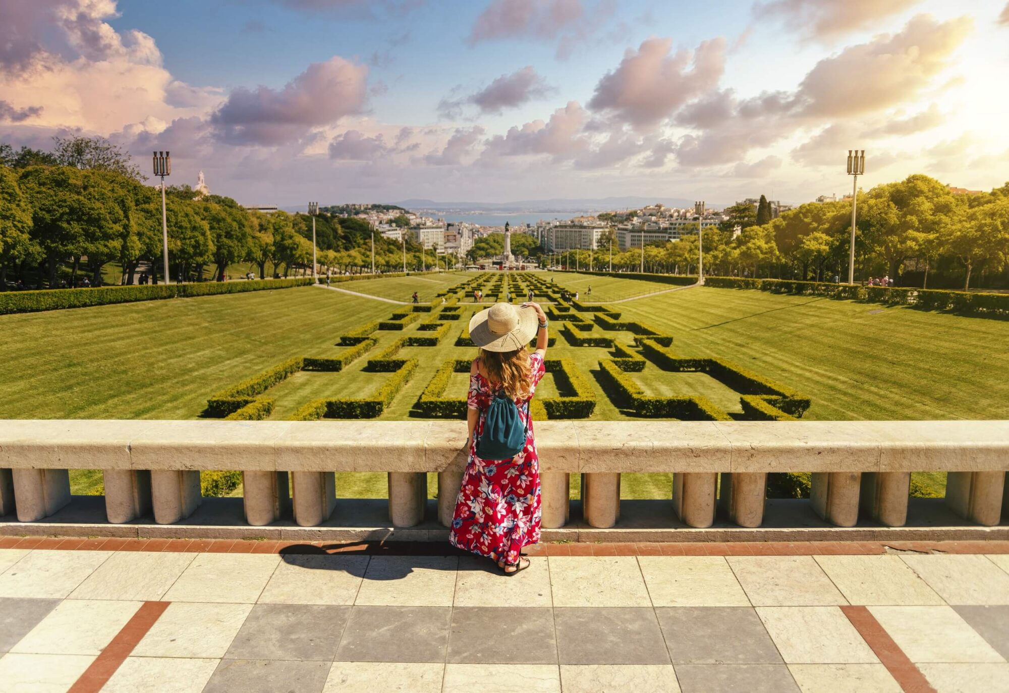 Jovem turista com vestido floral vermelho no Parque Eduardo VII, sob a luz do sol, em Portugal
